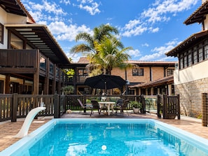 A swimming pool with a wooden deck, outdoor furniture, and a palm tree in the background. - Pousada Baleia Franca - Ferrugem/sc (Garopaba)