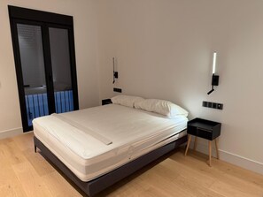 A modern bedroom with a bed, a nightstand, a wall-mounted light, and a sliding door to a balcony. - New Listing (Sanlúcar de Barrameda)