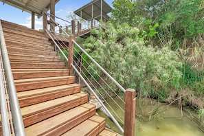Eine Holztreppe führt zu einer überdachten Aussichtsplattform mit Metallgeländern, umgeben von dichter Vegetation und einem Gewässer.