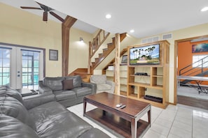 Ein Wohnzimmer mit einer Ledersofa, einem Holztisch, einem Fernseher auf einem Holzständer und einer Treppe mit hölzernen Geländern.