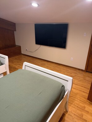 Ein Schlafzimmer mit einem Bett, Holzboden, Wandfernseher und einer hölzernen Bank.