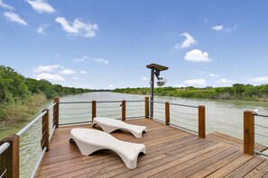Eine Holzterrasse mit zwei weißen Liegestühlen mit Blick auf einen Fluss.