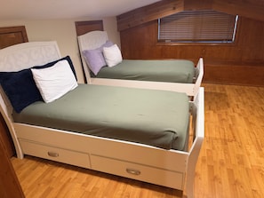 Ein Schlafzimmer mit zwei Betten, Holzboden, einem Fenster mit Jalousien und einer Tür mit einer Nummer.