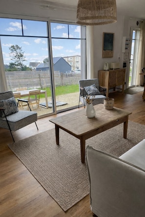 A spacious living room with a large sliding glass door leading to a backyard, a wooden coffee table, and a modern sofa. - New Listing (Barneville-Carteret)