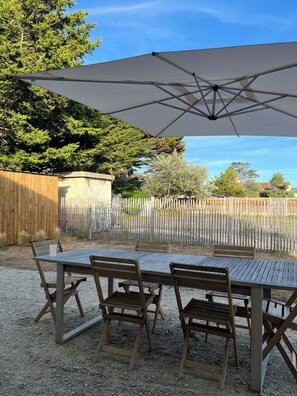 An outdoor patio with a wooden table and chairs, a large umbrella, and a gravel ground. - New Listing (Barneville-Carteret)