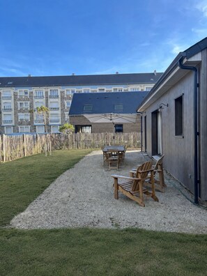 A patio area with a table and chairs, a wooden fence, and a building with a dark roof in the background. - New Listing (Barneville-Carteret)