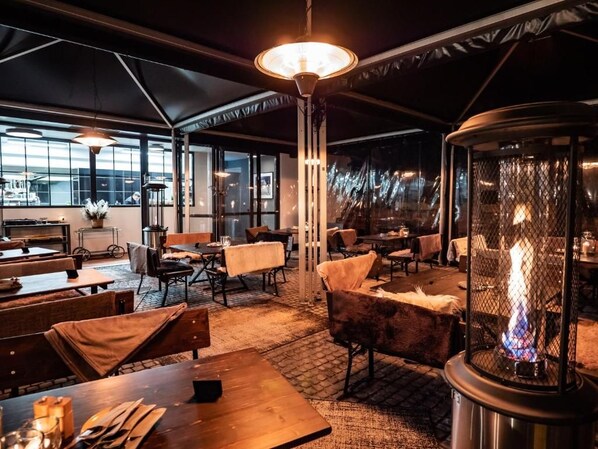 An indoor dining area with tables, chairs, and a central fire feature.