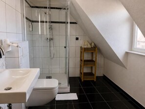 A bathroom with a shower, toilet, sink, and a wooden shelf. - Steinhaus1718 (Büdingen)
