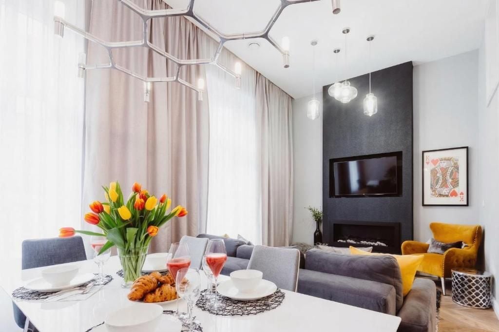 Un salon moderne avec un canapé, un téléviseur à écran plat fixé au mur et un coin repas avec une table mise pour deux personnes.