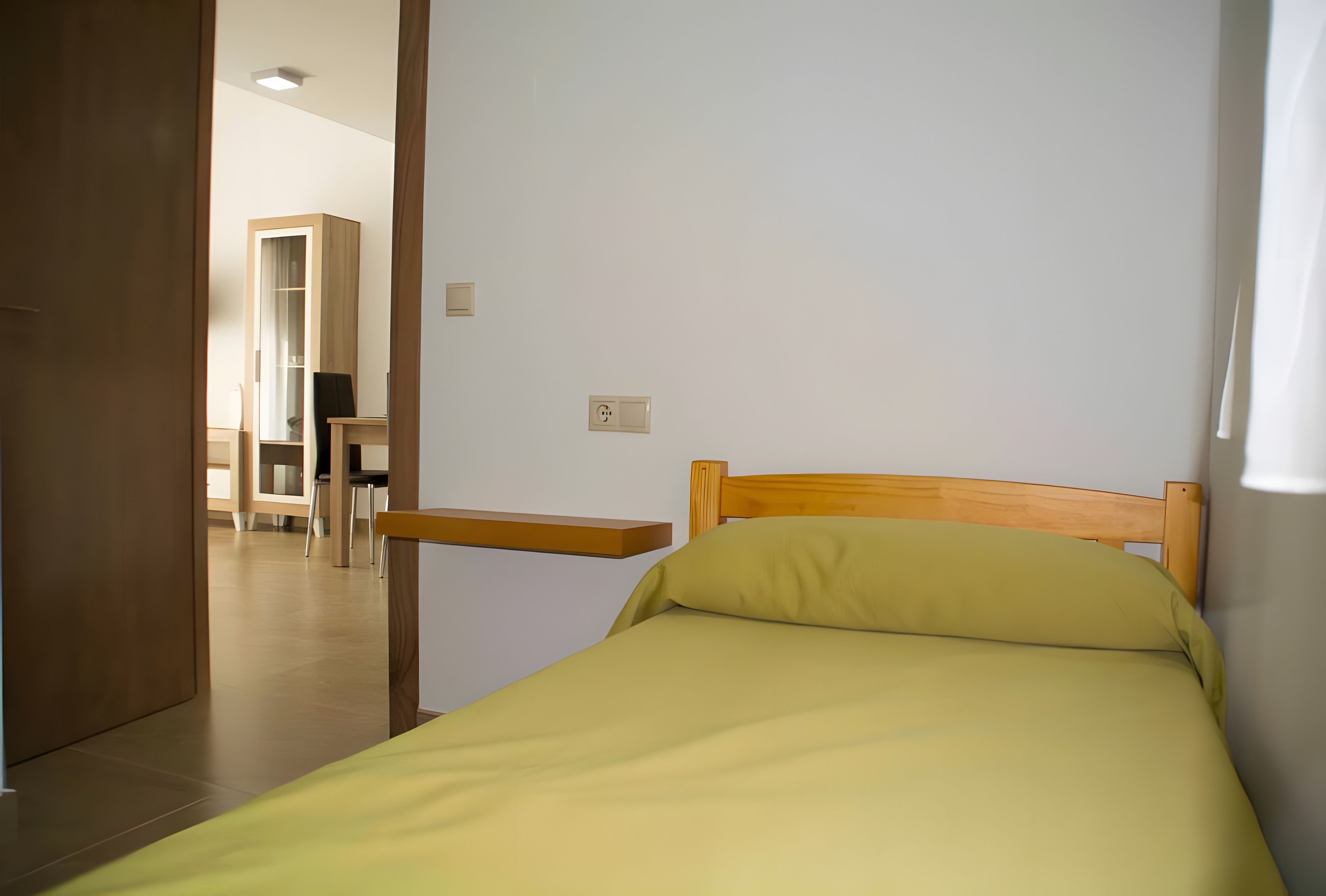 A single bed with a wooden headboard and a green pillow in a room with white walls.