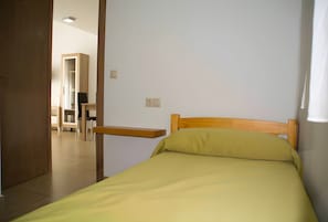 Una cama individual con cabecera de madera y almohada verde en una habitación con paredes blancas.