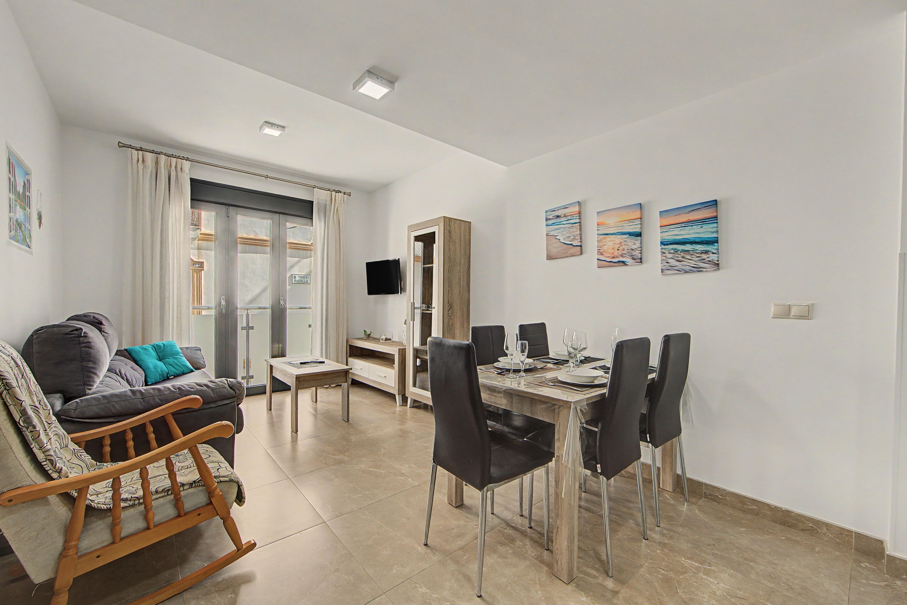 Een moderne woonkamer met een bank, een eettafel voor vier personen en een aan de muur bevestigde televisie.