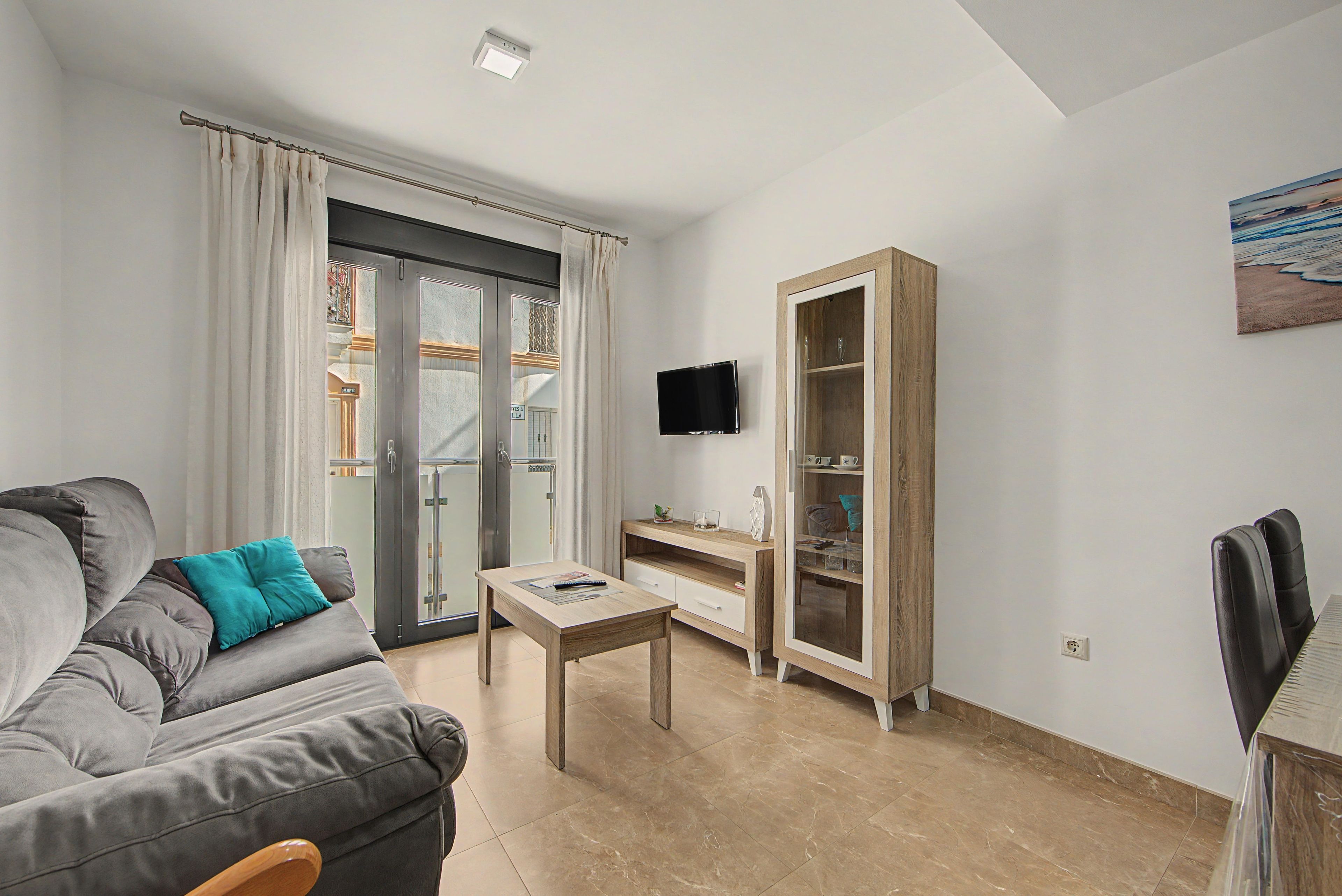 Een moderne woonkamer met een grijze bank, een houten kast en een flatscreen televisie aan de muur.