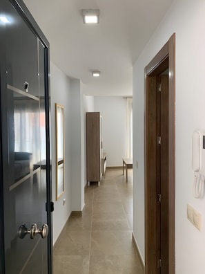 Un pasillo de hotel con una puerta de madera, un espejo, un teléfono y un banco.