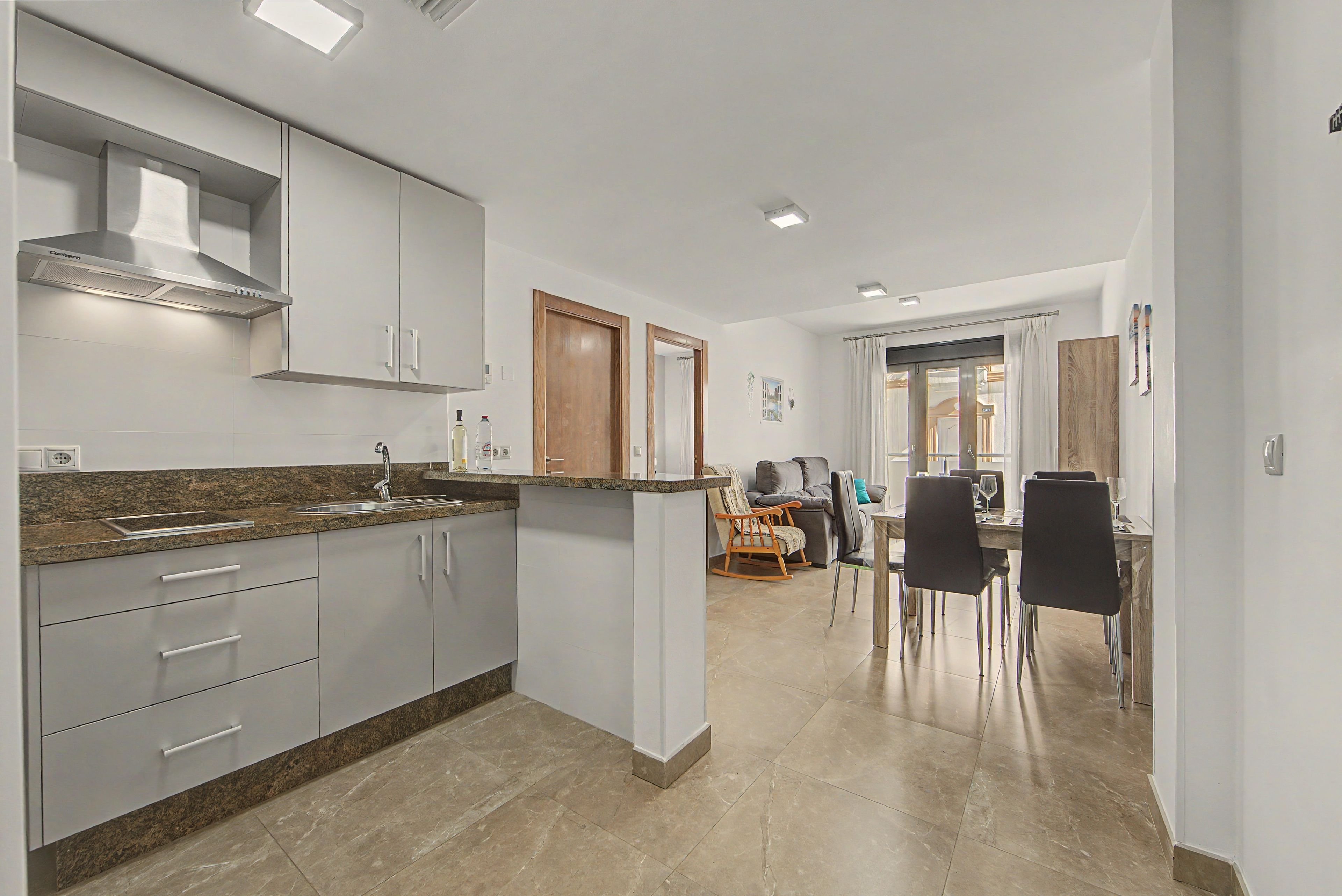 Een moderne keuken met granieten aanrechtbladen, roestvrijstalen apparatuur en een eethoek met een tafel en stoelen.