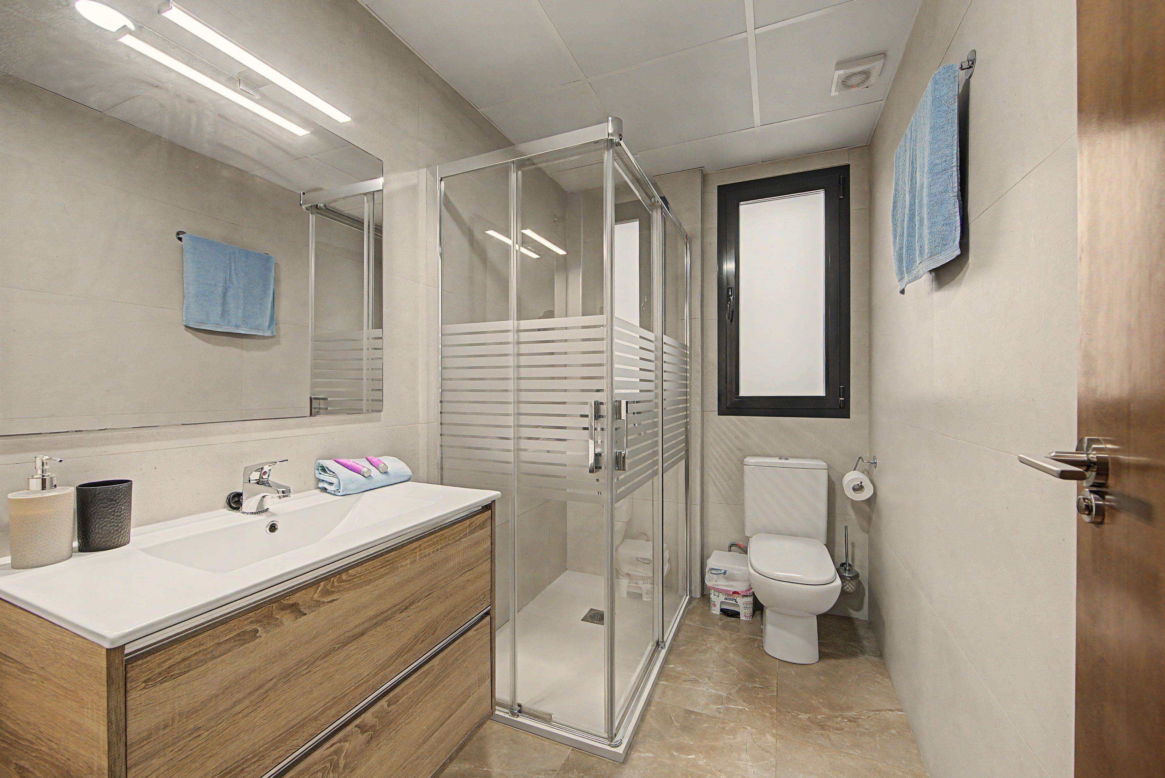 Een moderne badkamer met een douche met glazen wand, een houten wastafelmeubel, een toilet en een handdoekhouder.