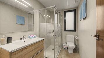Een moderne badkamer met een douche met glazen wand, een houten wastafelmeubel, een toilet en een handdoekhouder.
