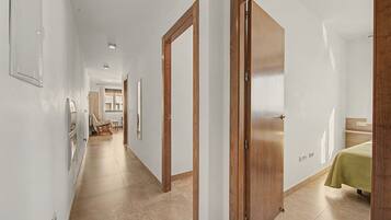 Un pasillo con puertas de madera, una cama con cubrecama verde y un baño a lo lejos.