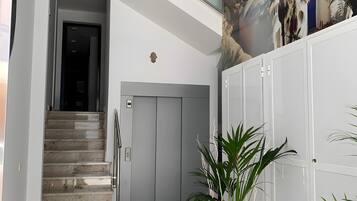 A modern interior with a staircase leading to an elevator, a welcome mat with cacti, and a mural of a beach scene.