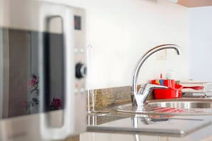Een keuken met een roestvrijstalen spoelbak, een magnetron en een rode afwasslede.