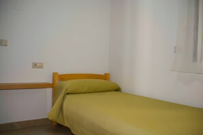 Een kleine kamer met een enkel bed, een houten hoofdbord en een groene sprei.