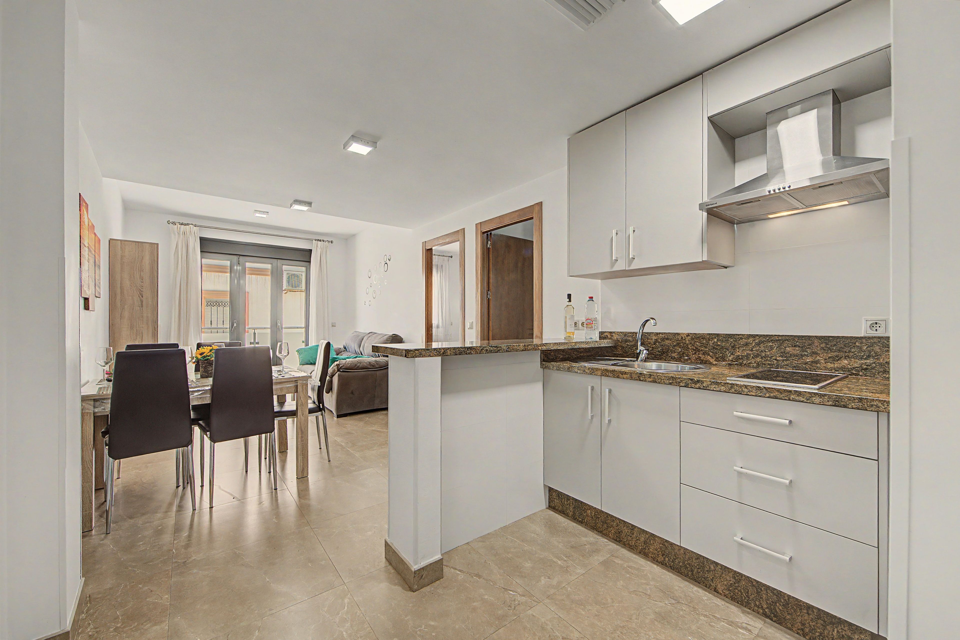 A modern kitchen with white cabinets, a granite countertop, and a stainless steel range hood.