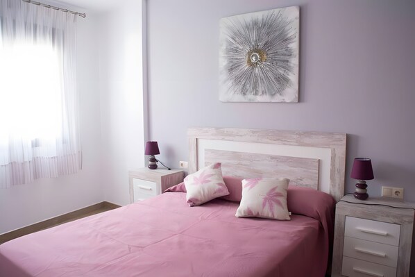 Een slaapkamer met een bed, twee nachtkastjes, een lamp en een kunstwerk aan de muur.