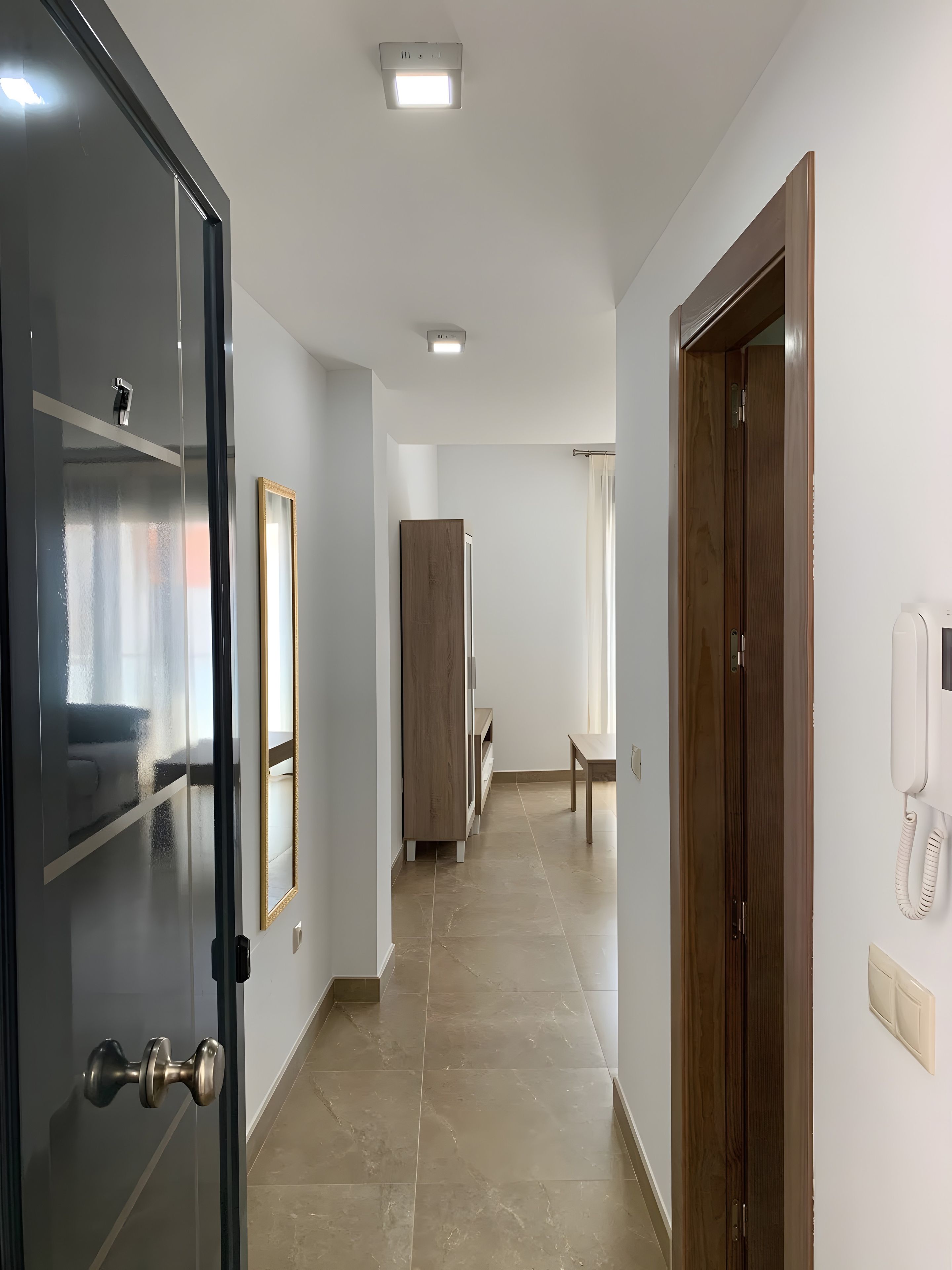 A hotel corridor with a wooden door, a mirror, a telephone, and a bench.