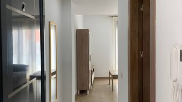 A hotel corridor with a wooden door, a mirror, a telephone, and a bench.
