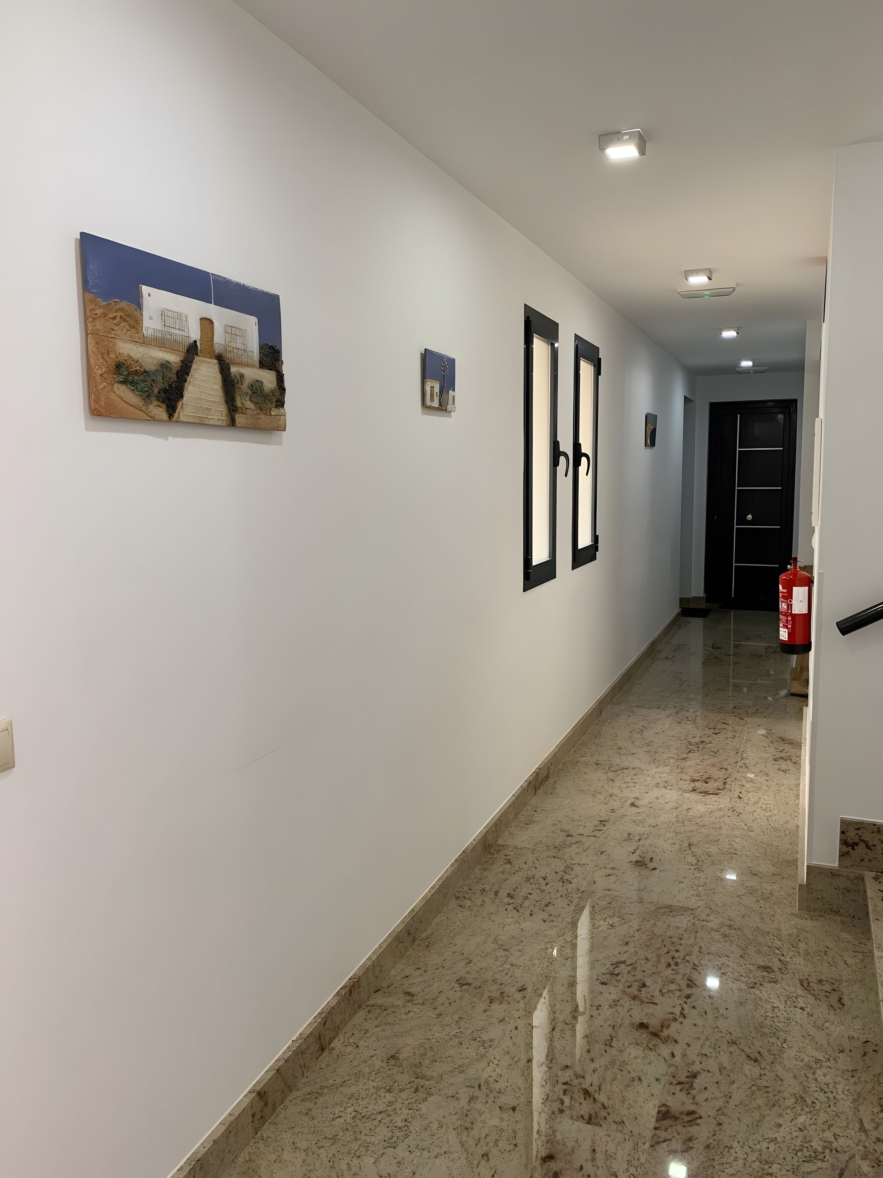 A hallway with white walls, a marble floor, and two framed pictures on the wall.