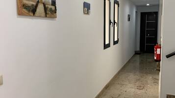 A hallway with white walls, a marble floor, and two framed pictures on the wall.