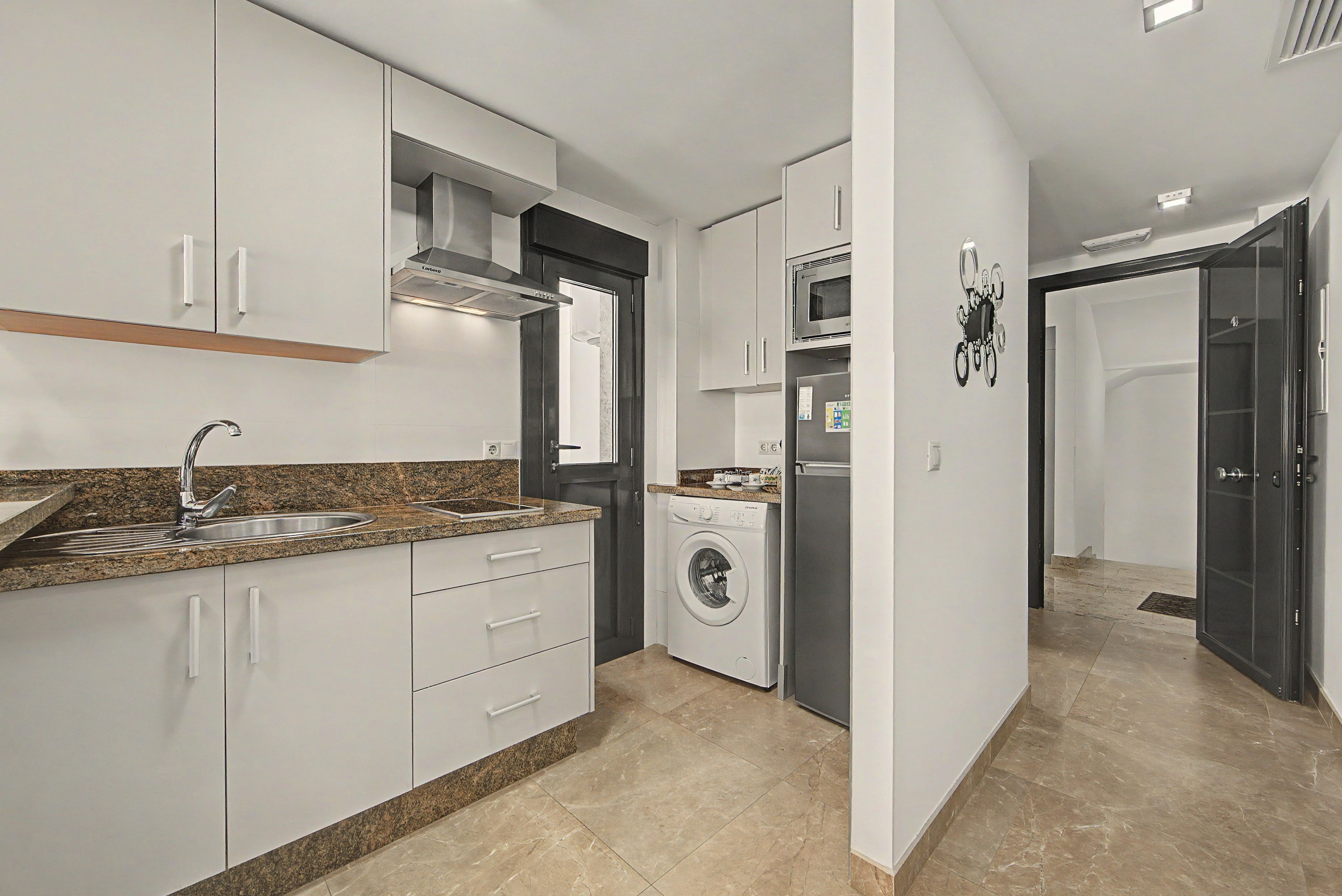 Een moderne keuken met witte kasten, een granieten aanrecht, een roestvrijstalen spoelbak, een ingebouwde oven en een wasmachine.