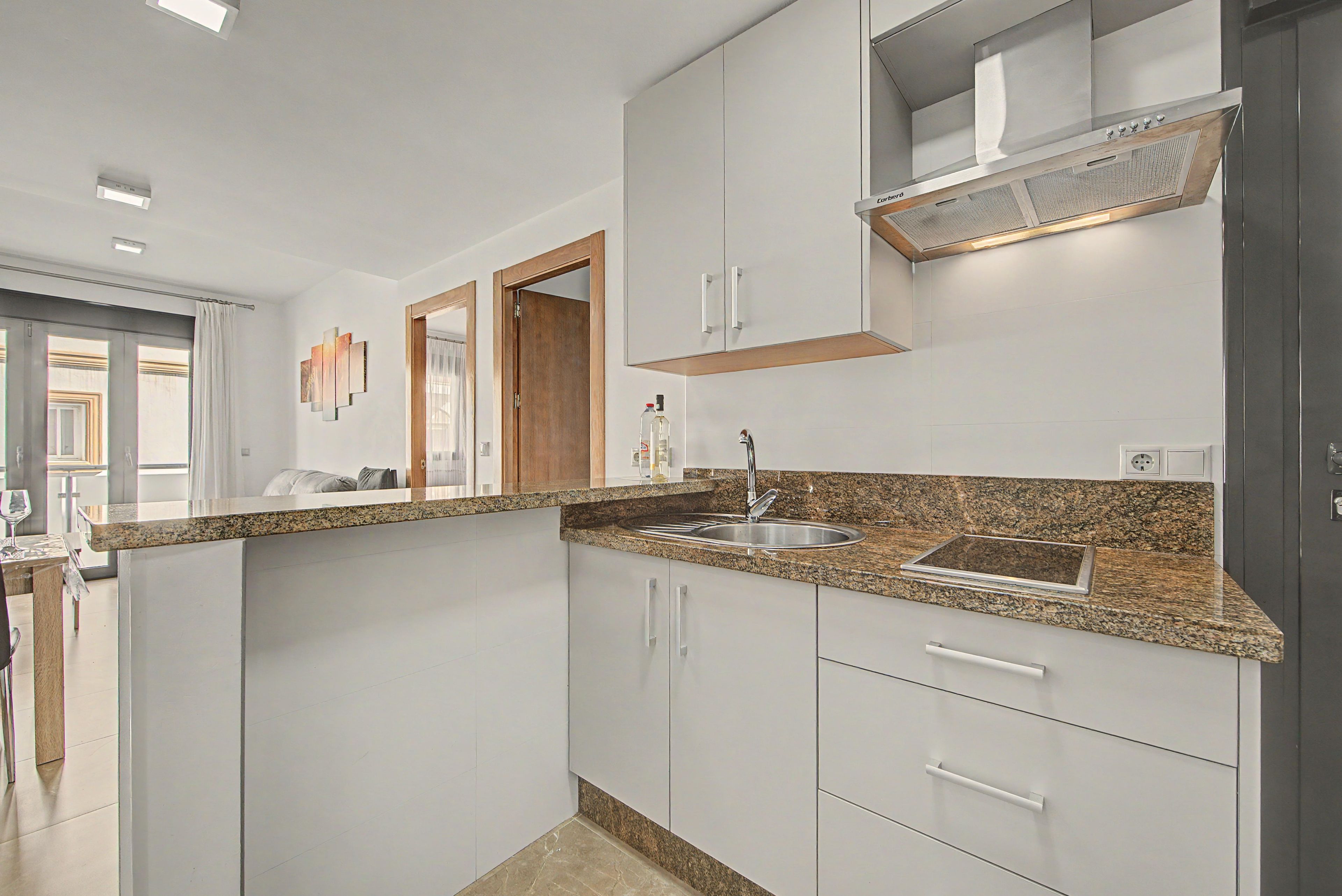 Een moderne keuken met witte kasten, granieten aanrecht en roestvrijstalen apparatuur.