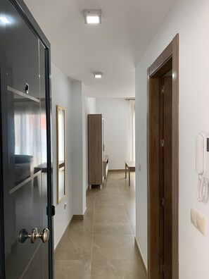 Een hotelgang met een houten deur, een spiegel, een telefoon en een bankje.