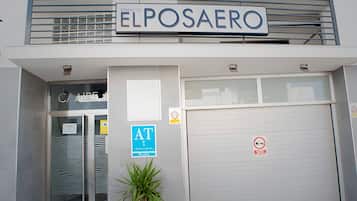 Een gebouw met een bord met de tekst 'ELPOSAERO' boven de ingang, een glazen deur, een blauw 'AT'-bord en een rookvrij-bord op de garagedeur.