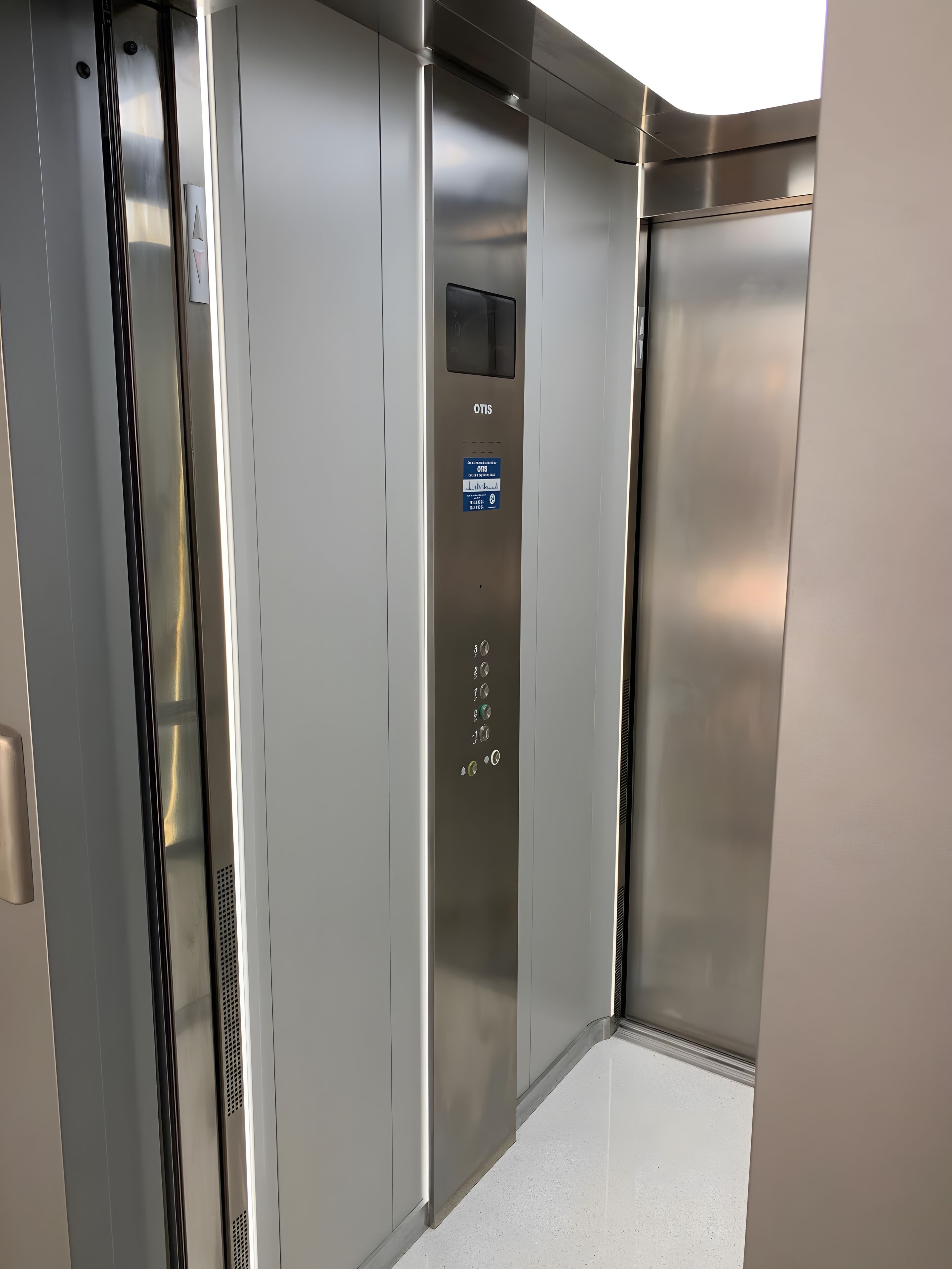 An elevator interior with a metallic finish, a control panel with buttons, and a sign indicating the elevator's name.