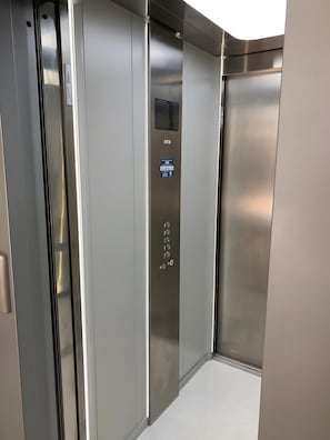 L’intérieur d’un ascenseur est doté d’une finition métallique, d’un panneau de commande avec des boutons et d’une plaque indiquant le nom de l’ascenseur.