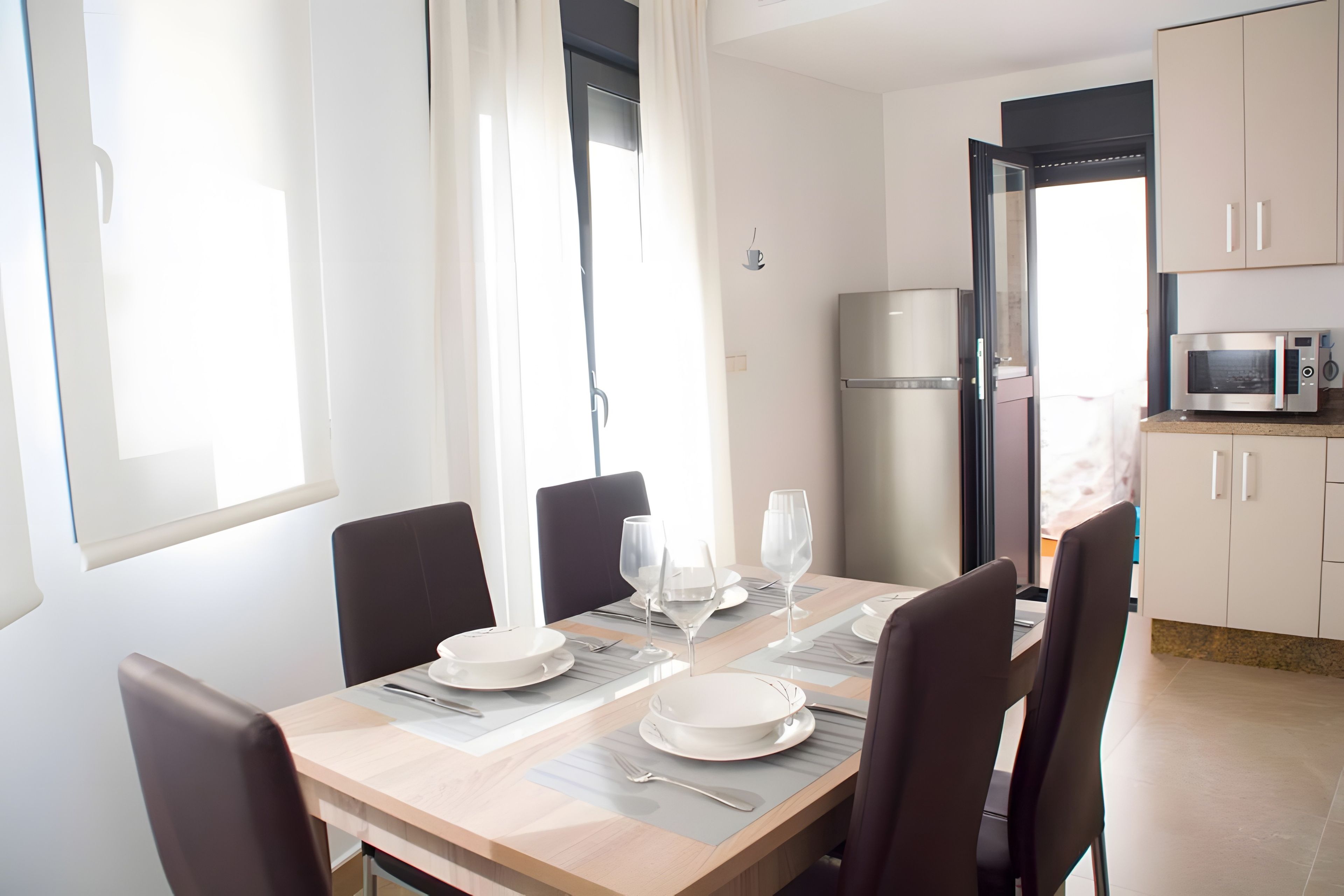 A dining area with a table set for four, chairs, a refrigerator, and a microwave.