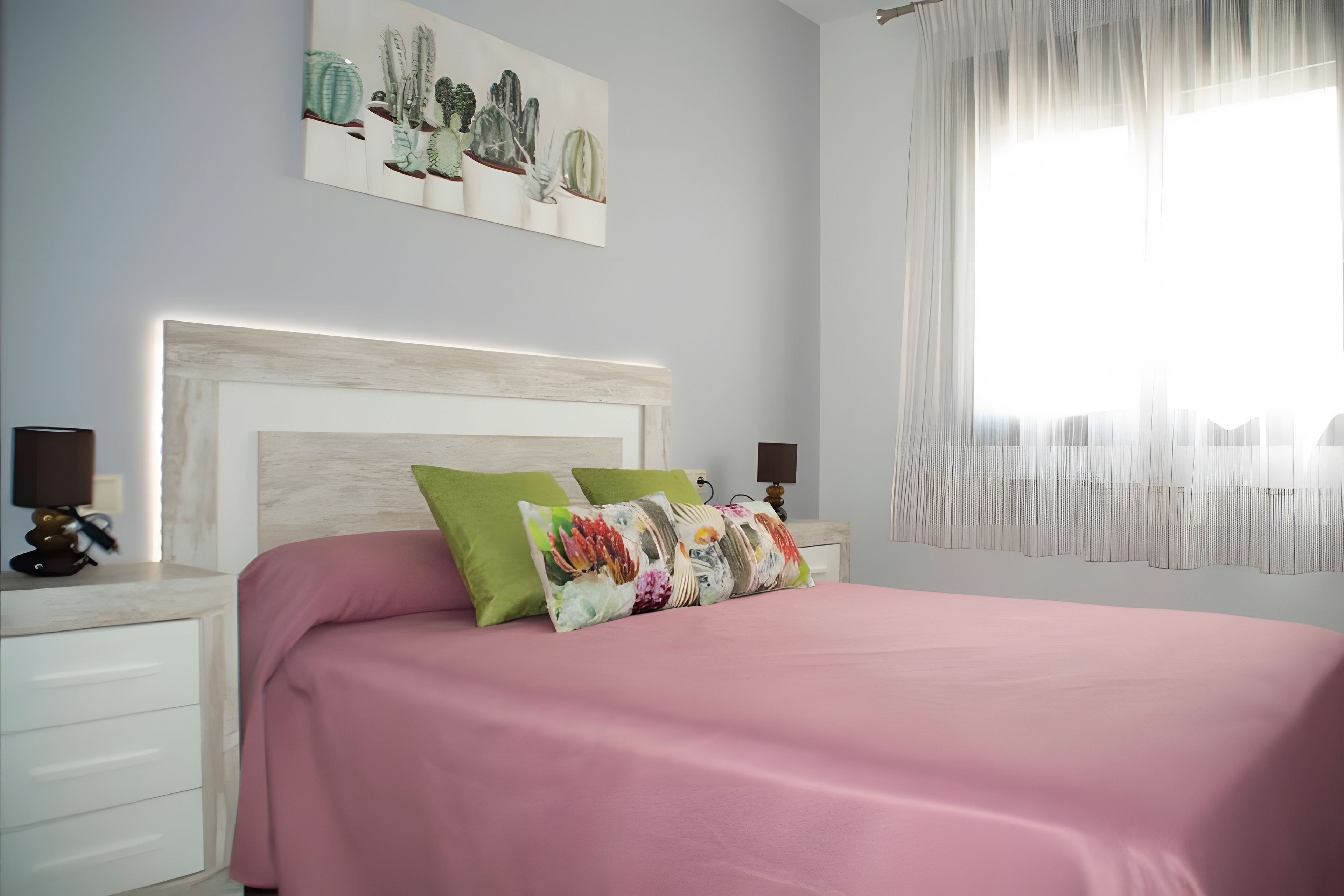 A bedroom with a bed, pillows, a nightstand, a lamp, a wall art piece, and a window with curtains.