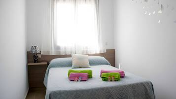 A bedroom with a bed, a nightstand, a lamp, and a window with sheer curtains.