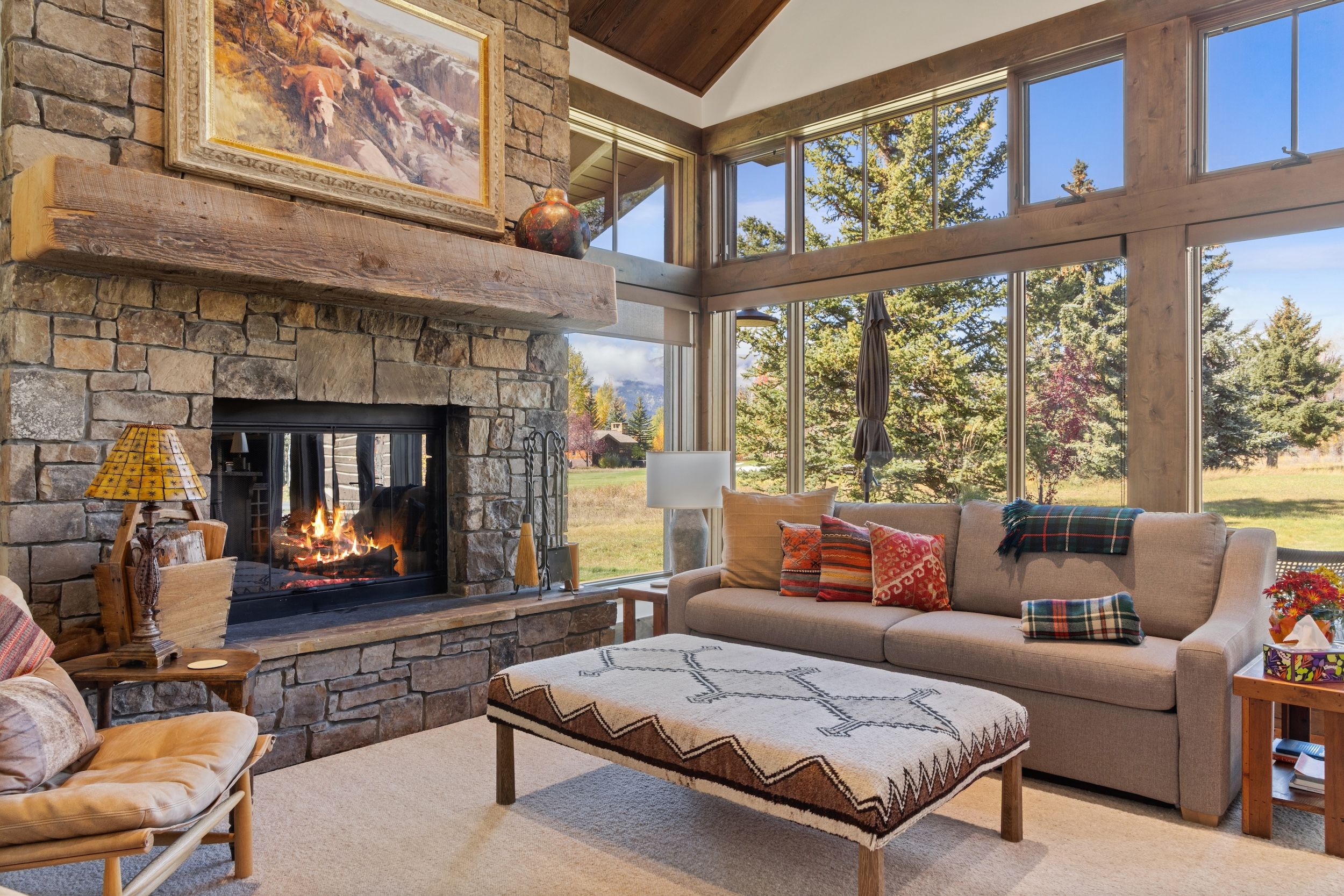A cozy living room with a stone fireplace, a comfortable sofa, and a large window offering a view of the outdoors.