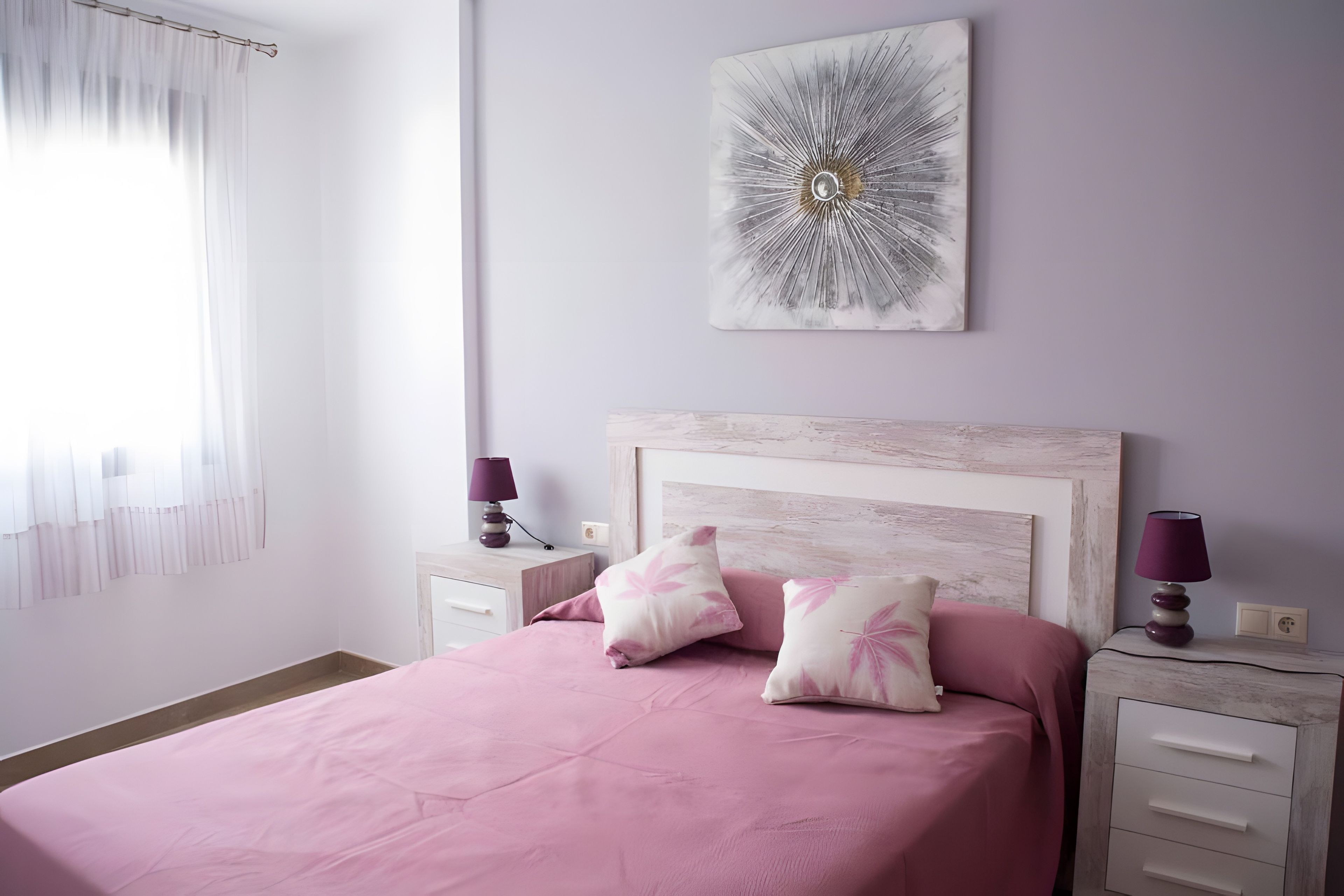 A bedroom with a bed, two bedside tables, a nightstand, a lamp, and a wall-mounted artwork.