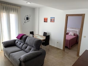 Een moderne woonruimte met een bank, een eettafel met stoelen en een bed met hoofdeinde.