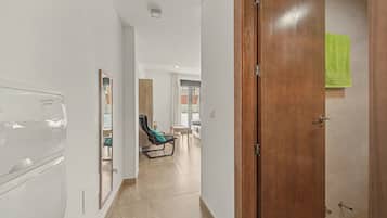 Un pasillo con una puerta de madera, un espejo, una silla y una cama a lo lejos.