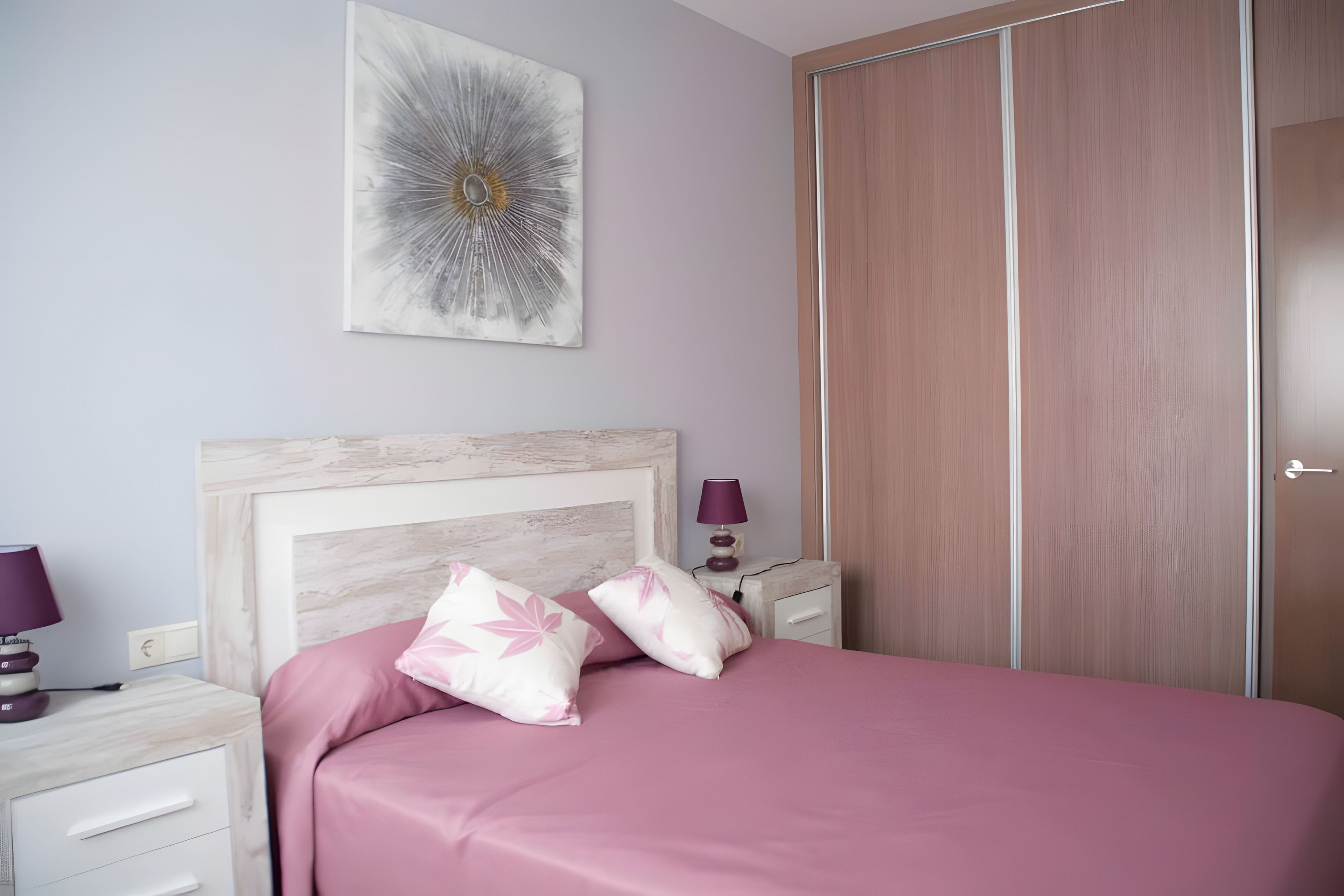 Een slaapkamer met een bed, nachtkastje, lamp en een kledingkast.