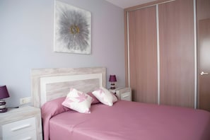 Een slaapkamer met een bed, nachtkastje, lamp en een kledingkast.