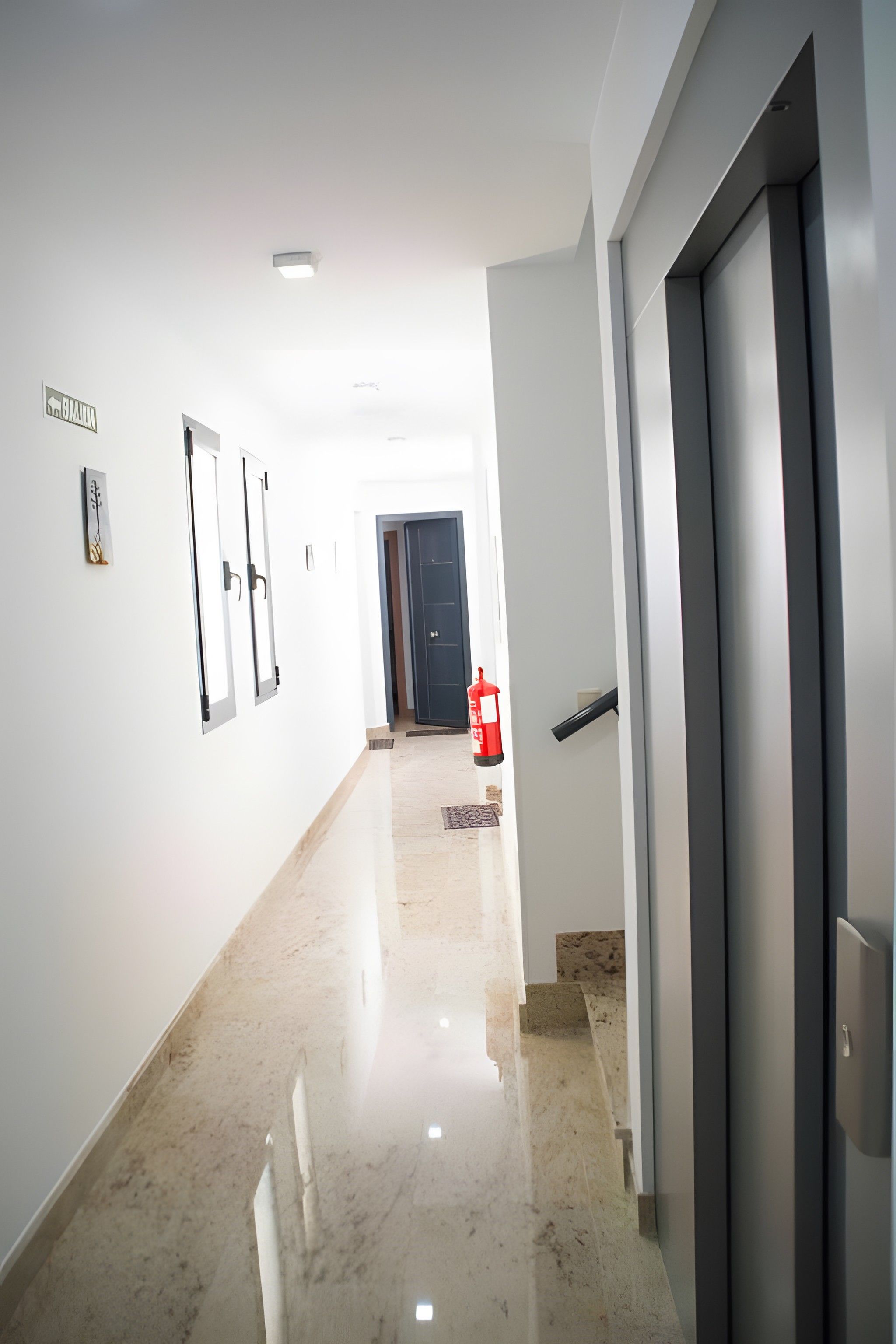 A hallway with a polished floor, a fire extinguisher, and a door on the right.
