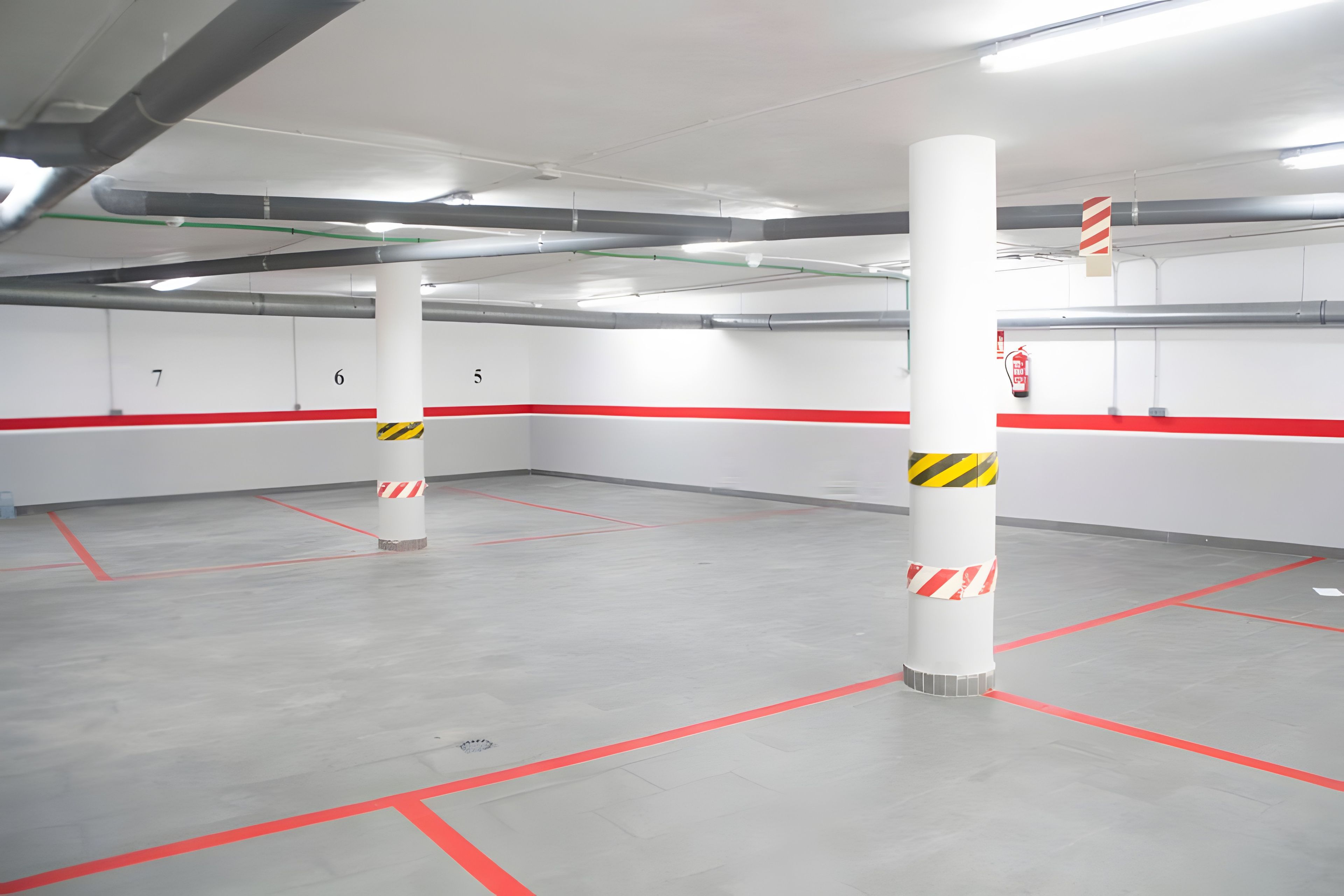 A parking garage with white walls, red safety lines, and columns with yellow and black stripes.