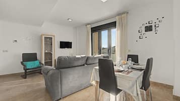 Una sala moderna con un sofá gris, una mesa de comedor para dos personas y un televisor montado en la pared.