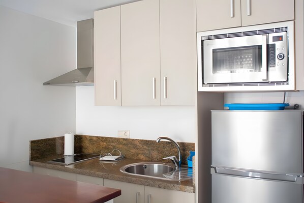 Een keuken met een roestvrijstalen koelkast, een magnetron en een gootsteen met een granieten werkblad.